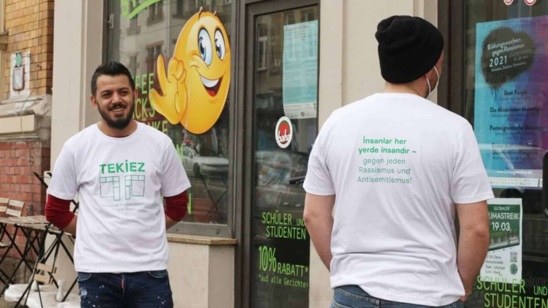 Zwei Personen tragen T-Shirts des tekiez und stehen vor einer Eingangstür