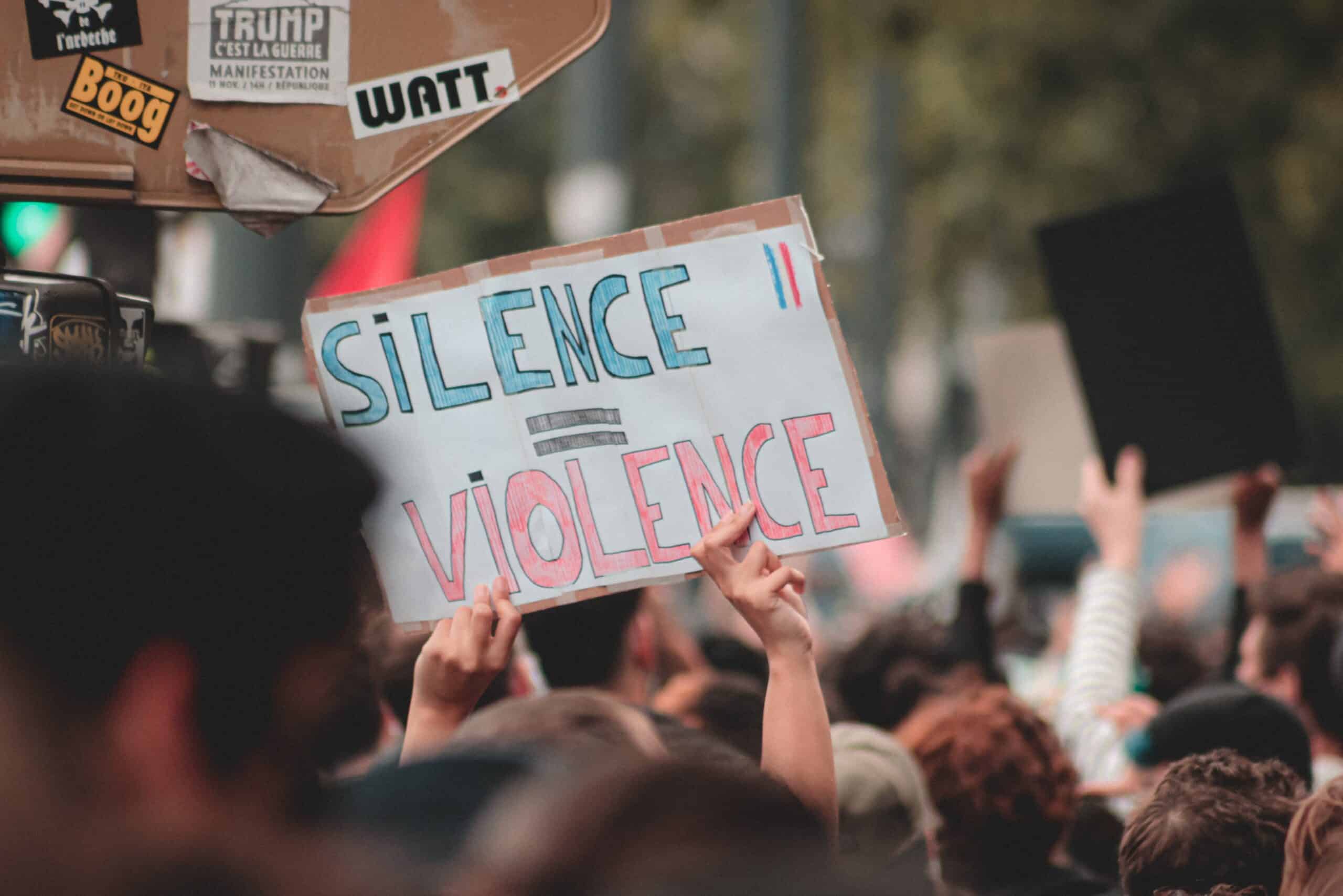 Eine Person hält ein Schild hoch. Auf diesem steht: Silence = violence