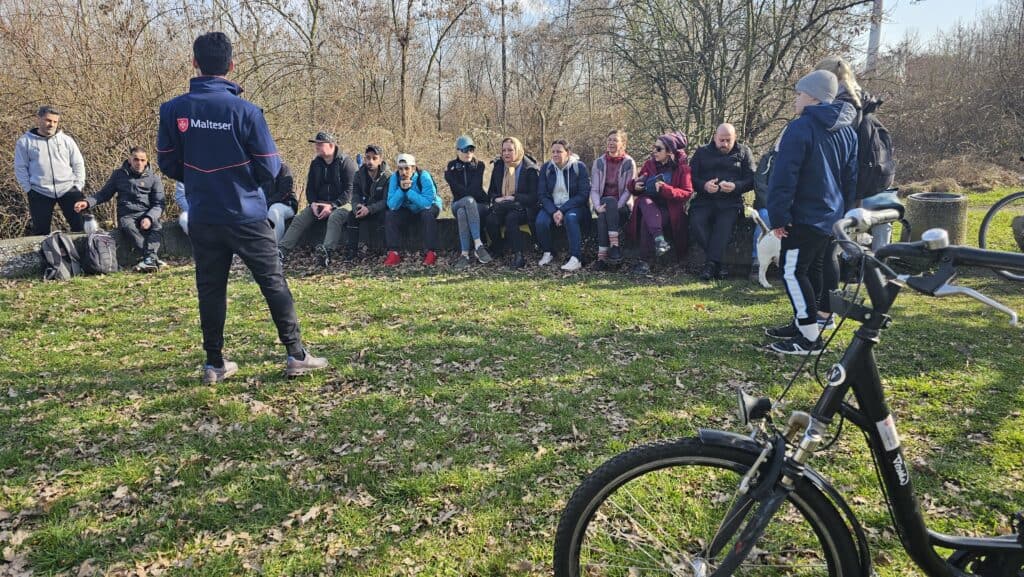 Menschen sitzen nebeneinander auf einem Baumstamm, Fahrräder sind zu sehen.